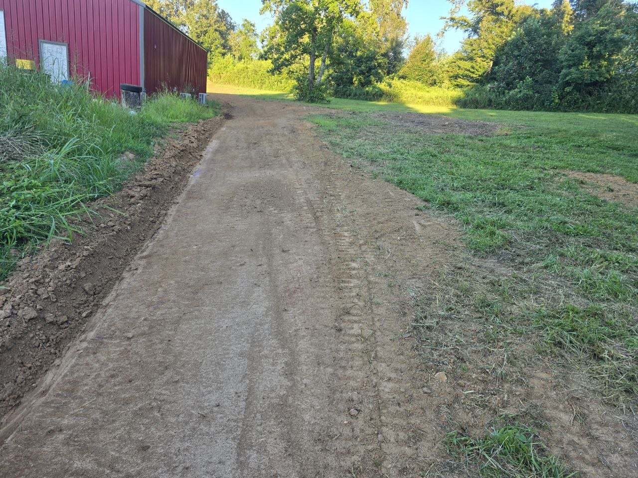 Graded dirt track leading toward a red barn