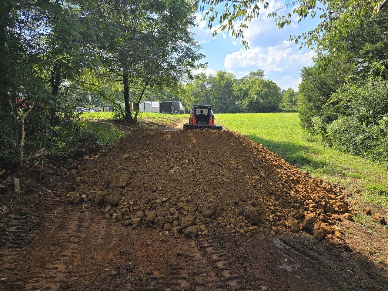 Kubota track loader placing and shaping fill along a wooded access lane