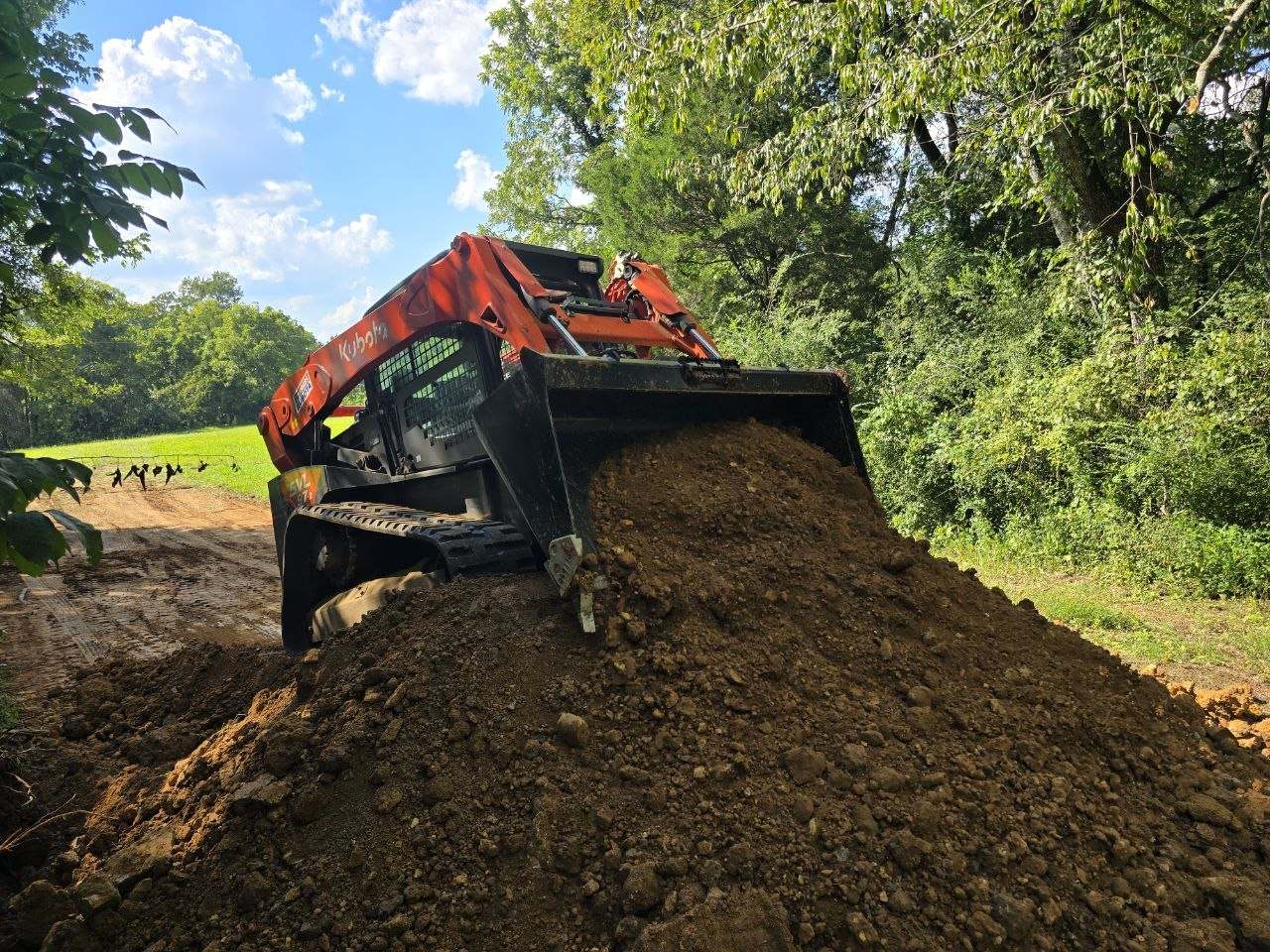 Orange Kubota SVL97-2 lifting a full bucket of dirt from the top of a large mound