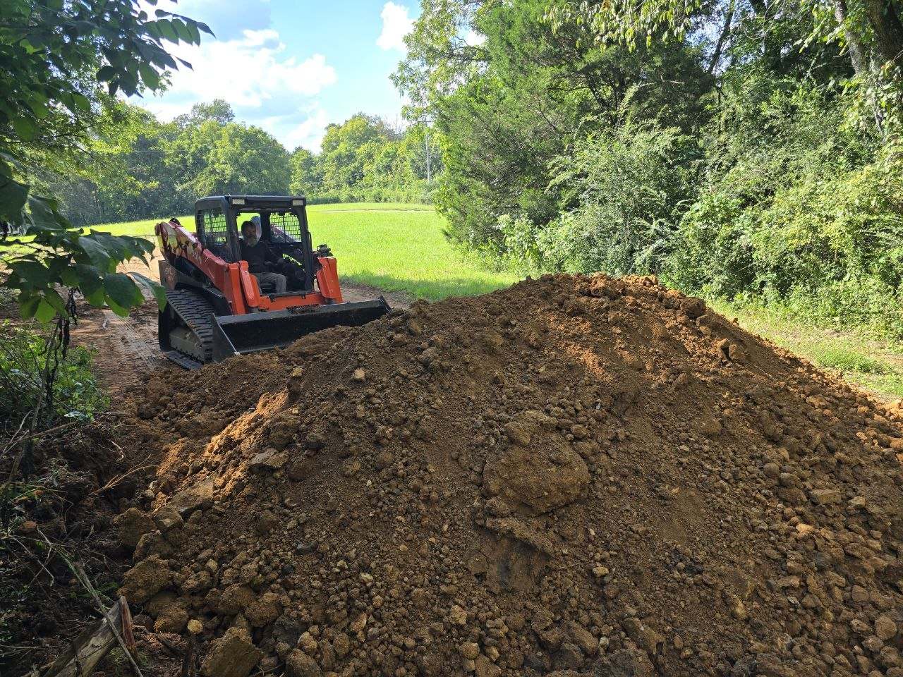 Orange Kubota SVL97-2 behind a large mound of dirt on a path through a field