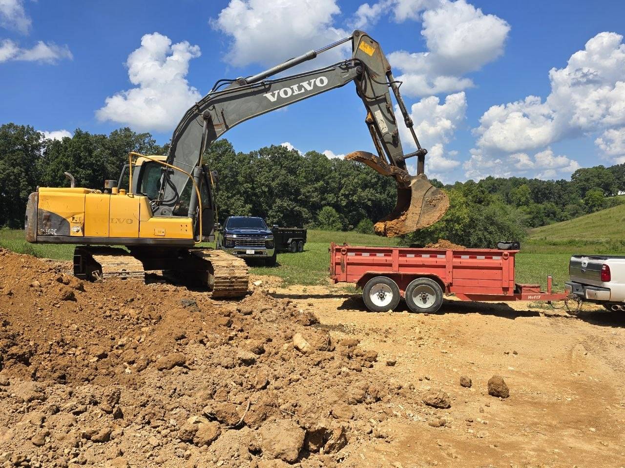 Excavator loading dirt into a dump trailer on a job site