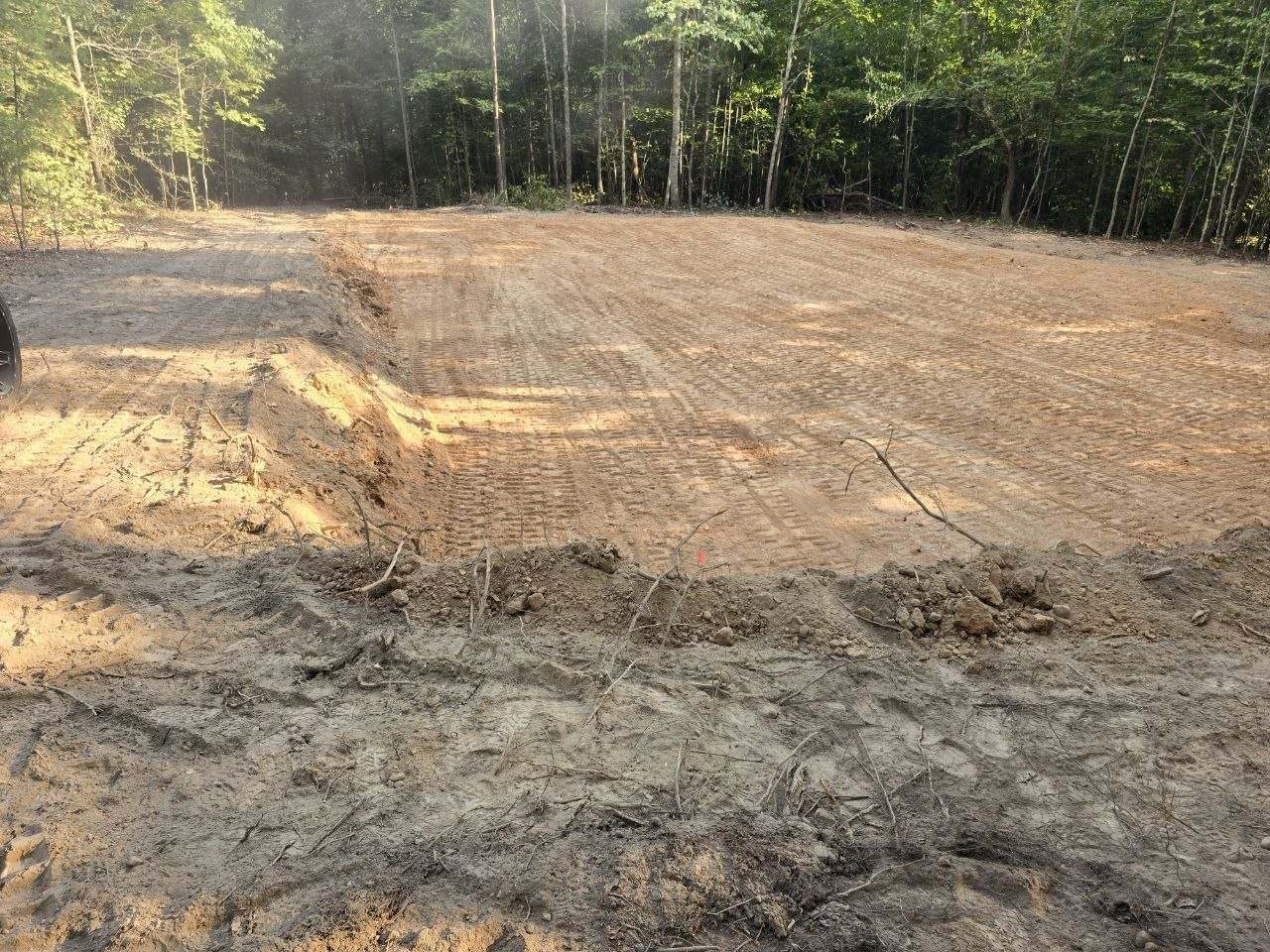 Finished building pad beside a rough embankment of cut dirt at the wood line