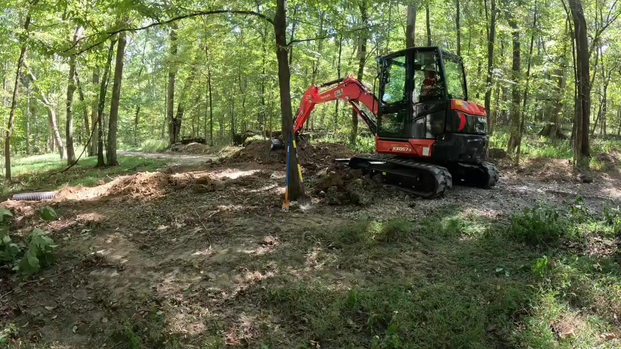 Kubota mini excavator working beside a culvert site on a wooded drive