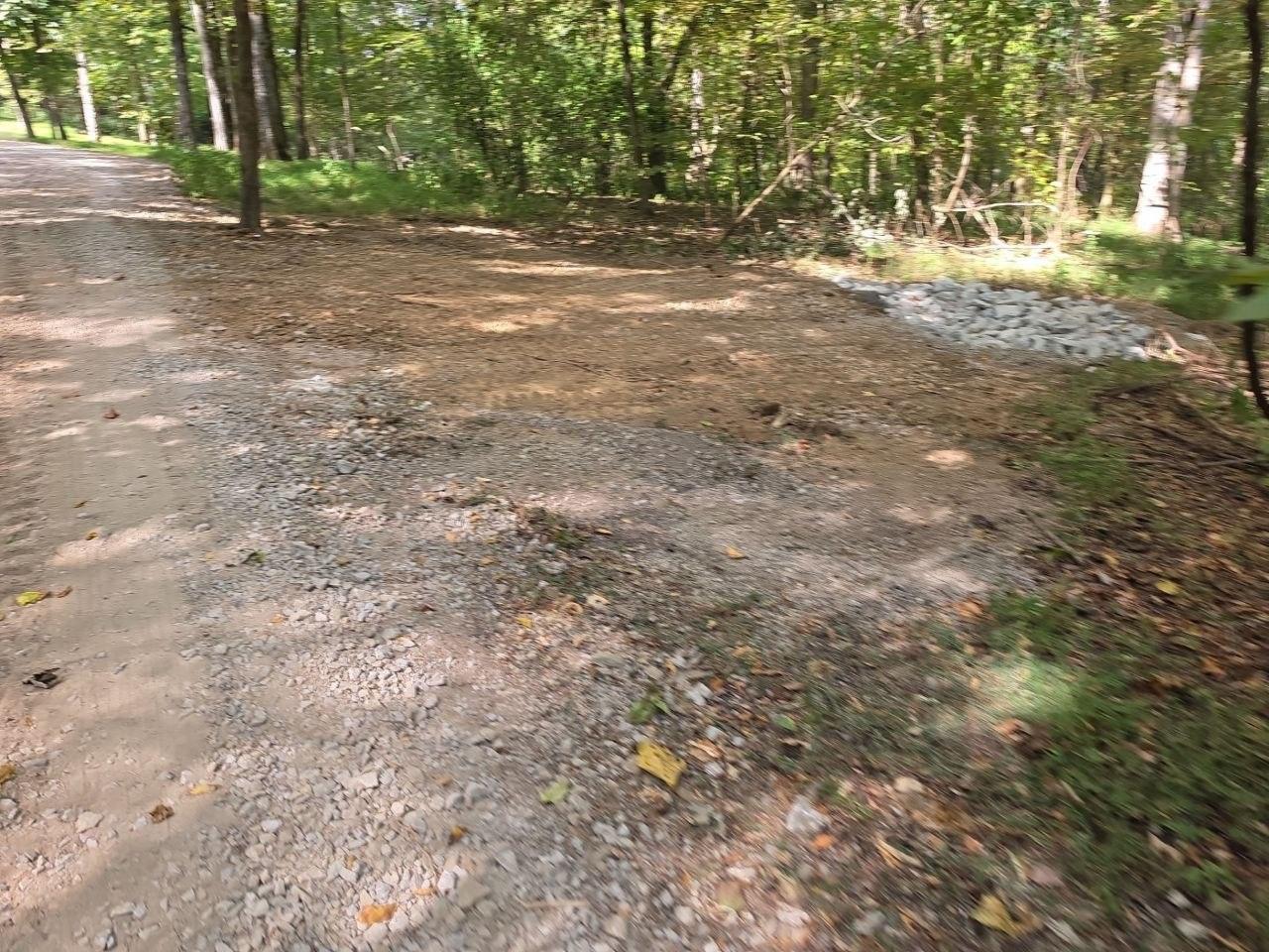 Gravel drive meeting a dirt turnoff, with a pile of rip rap stone beside it