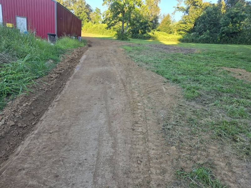 Freshly graded lane with a drainage ditch beside a farm building