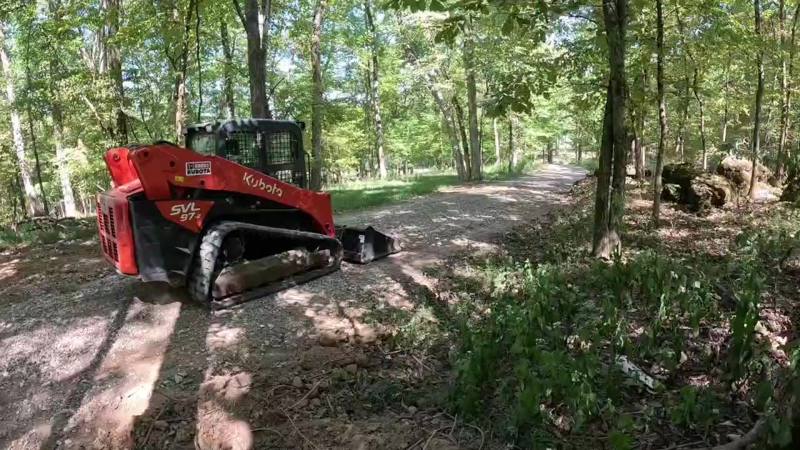 Skid steer grading a dirt drive through the woods
