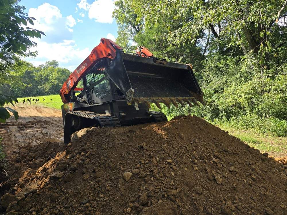 Orange Kubota SVL 97 track loader working a large mound of dark brown fill dirt